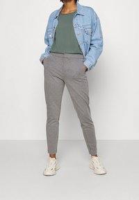 Jeansowa kurtka, zielona bluzka i szare spodnie w tapered. Sneakersy w jasnym kolorze. Gładkie tekstury i swobodne elementy designu w całym zestawie.