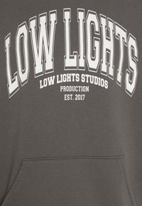 Felpa con cappuccio grigia scura con testo bianco in evidenza: "LOW LIGHTS," "LOW LIGHTS STUDIOS," "PRODUCTION," e "EST. 2017," con tasca frontale.