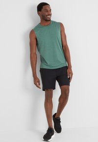 Green sleeveless shirt paired with black shorts. The shirt has a soft texture, while the shorts are made of lightweight material. Black sneakers complete the look.