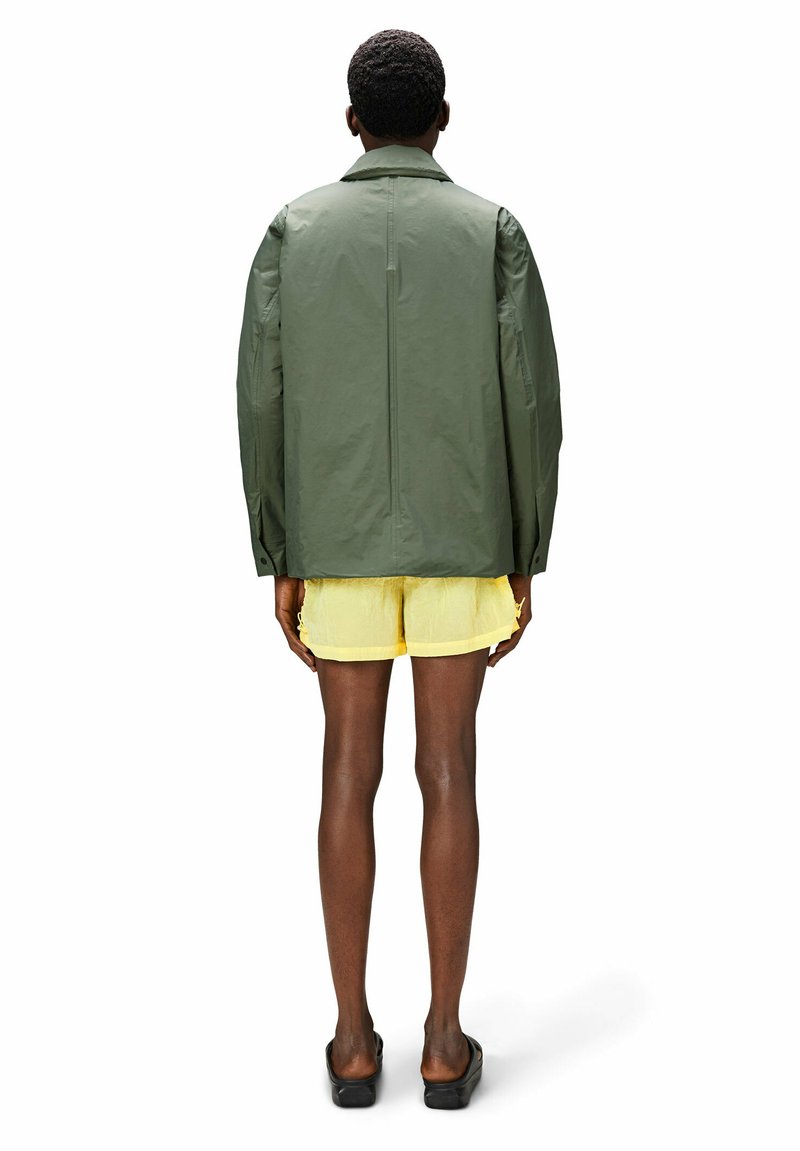 Veste verte à manches longues avec une coupe décontractée, vue de dos, associée à un short jaune. Texture lisse et détails de design simples.