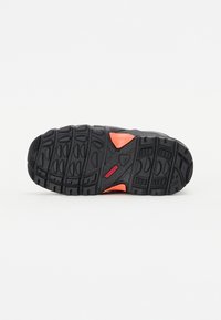 Black hiking shoe sole with textured rubber, featuring deep tread patterns, a central orange accent, and a red logo at the heel.