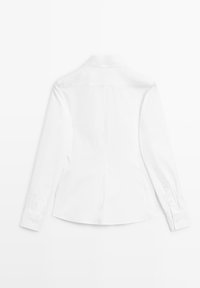 Chemise blanche à manches longues avec boutons et col, vue de dos, étalée à plat sur un fond blanc.