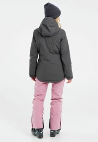 Grau wasserfeste Jacke mit Kapuze, getragen über rosa Skihosen. Beide Kleidungsstücke zeichnen sich durch glatte Texturen und praktische Designs für die Winterbekleidung aus.