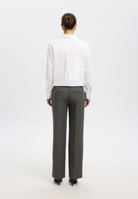 Biela košeľa s golierom a manžetami na gombíky, doplnená o šité šedé nohavice s vysokým pásom. Jemná látka s jemným vzorom, úzky strih.