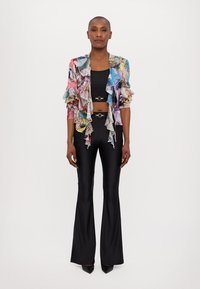 Värikall, mönstrad cropped jacka med volanger, bärs över en svart crop top. Svarta vida byxor med slät textur, ihop med spetsiga svarta klackar.
