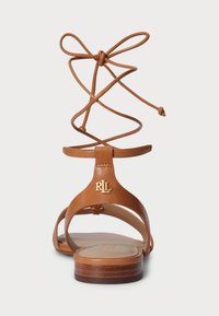 Καφέ δερμάτινο σανδάλι με κοπές στο σχέδιο και σταυρωτές λεπτομέρειες με κορδόνια. Έχει το λογότυπο RLL στη φτέρνα και επίπεδη ξύλινη σόλα.