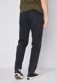 Melni džinsi ar taisnu piegulšanu, piecu kabatu dizainu un smalku tekstūru. Valkāti ar melniem augstiem kedām.