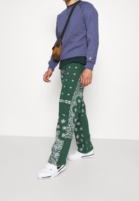 Pantalones de mezcla de algodón con un patrón de pañuelo verde, combinados con un sudadera morada. El calzado son zapatillas blancas. Bandolera pequeña marrón.