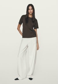 Brun t-shirt med korte ærmer parret med brede hvide bukser. Outfittet har et simpelt design uden synlige mønstre eller detaljer.