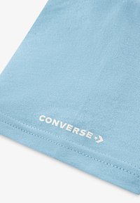 Svijetloplati pamuk s glatkom teksturom, s bijelim logotipom "CONVERSE" i šavom duž ruba.