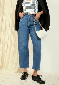 Jeans din denim albastru, de tipul high-rise, cu o croială relaxată, material texturat și detalii cusute. Asortați cu pantofi din piele patentată negri și o geantă albă.