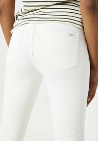 Vaqueros de denim blanco con un diseño ajustado, textura sutil y dos bolsillos traseros. El denim tiene un acabado suave y detalles de costura mínimos.