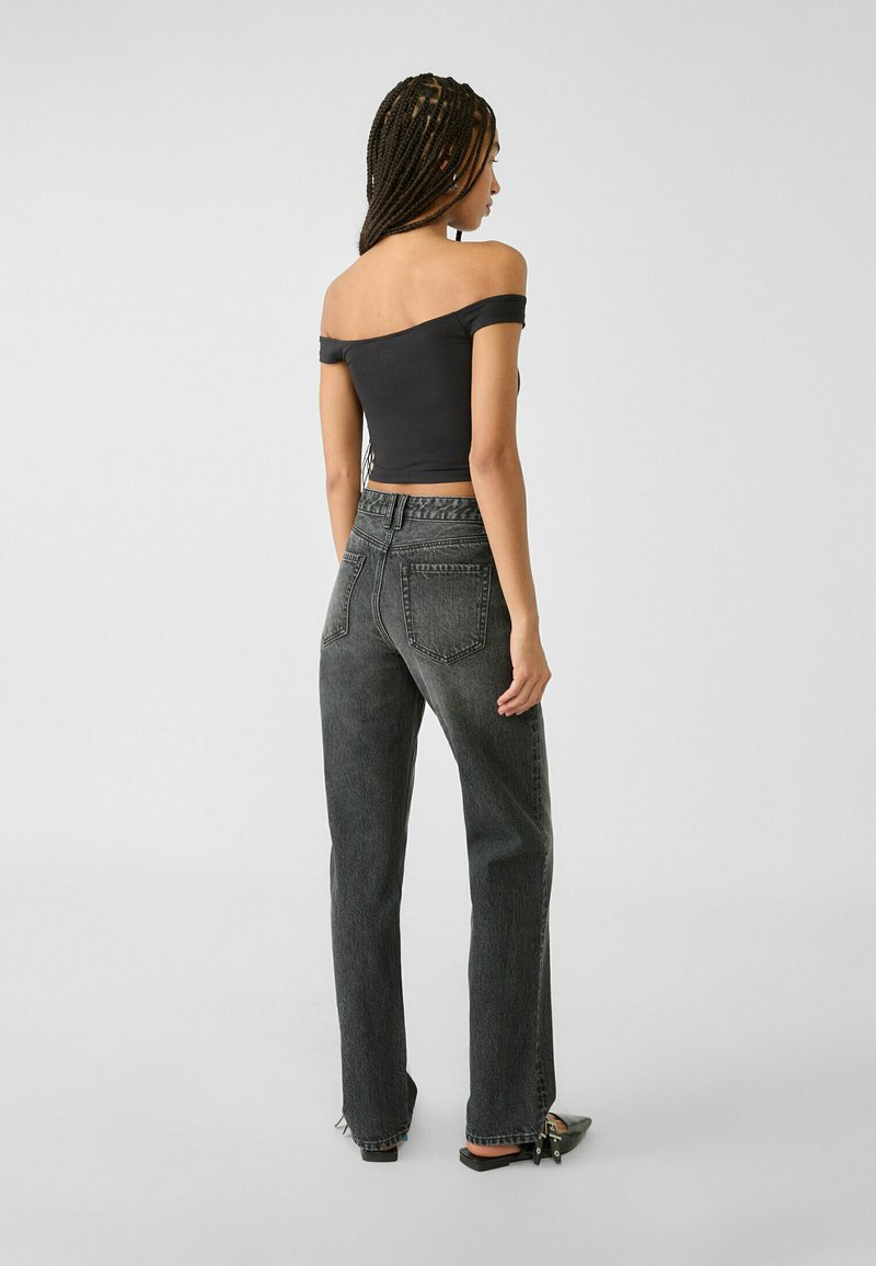 Top corto nero off-the-shoulder abbinato a jeans in denim grigio scuro a vita alta e dal taglio morbido. Tessuto liscio e dettagli di cucitura sottili.