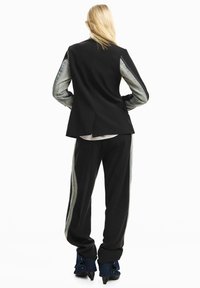 Giacca sartoriale nera con maniche in denim, abbinata a pantaloni neri con dettagli in denim. L'outfit presenta una silhouette moderna e un design strutturato.