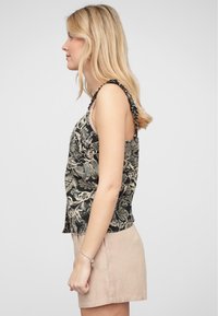 Top senza maniche nero con motivo floreale beige, con spalline a volant e una vestibilità ampia. Abbinato a pantaloni corti beige chiaro.