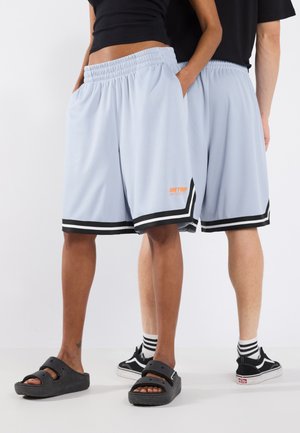 Pantaloni sportivi azzurri con vita elasticizzata, tasche laterali, bordi neri e dettaglio logo arancione. Indossati con calzature casual.