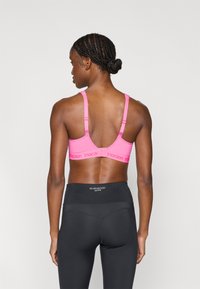 Ροζ αθλητικό σουτιέν με ρυθμιζόμενους ιμάντες, λεπτομέρειες από δίχτυ και λάστιχο με λογότυπο. Συνδυασμένο με μαύρο αθλητικό κολάν με ψηλή μέση.