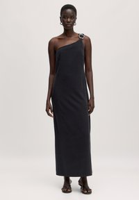 Schwarzes, einseitig tragbares Kleid mit sleeken, geradem Schnitt und silberner Schnalle am Ausschnitt. Hergestellt aus weichem Stoff, knöchellanges Design.