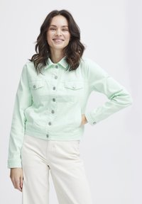 Chaqueta de mezclilla verde menta con cuello, botones delanteros y dos bolsillos en el pecho. Presenta un corte corto y mangas largas.