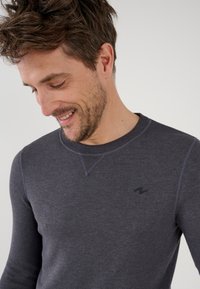 Maglietta a maniche lunghe di un grigio scuro realizzata in tessuto a costine, con scollo rotondo, cuciture in contrasto sottili e un piccolo logo nero sul petto.