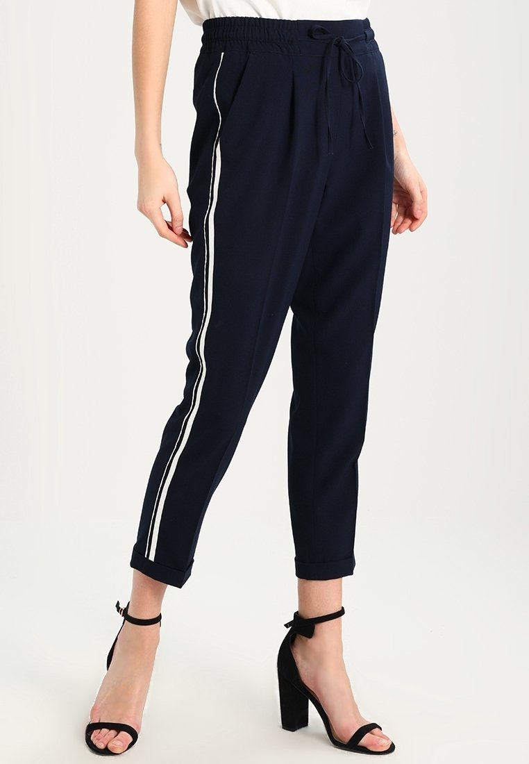 Granatowe zwężane spodnie z bocznymi paskami, elastycznym pasem i sznurkiem do regulacji. Materiał jest gładki, a krój luźny; zakończenie nogawki ma mankiety.