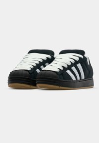 Black suede sneakers with white laces and three white stripes. Features a rubber toe cap and a gum sole for traction.
