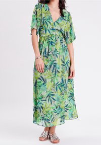 Robe maxi en tissu léger et transparent, avec un imprimé de feuilles vertes. Décolleté en V avec des manches courtes et volantes et une taille froncée.