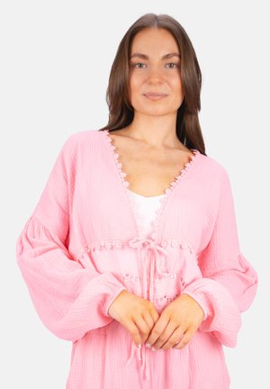 Blouse rose texturé avec un décolleté en V profond, bord en dentelle et détail à cordon. Les manches bouffantes longues ajoutent du volume à la coupe décontractée.