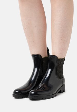 Botas de tobillo de goma negra con un acabado brillante, que cuentan con un panel lateral elástico dorado texturizado y un tacón bajo. Suela de goma duradera con dibujos.