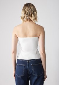 Hvit stroppeløs topp med en tettsittende overdel, parret med mørkeblå høyhåndte denimjeans med baklommer og kontraststing.