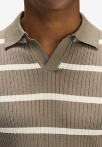 Beige kortärmad polo med V-ringning, med vertikal ribbning och horisontella vita ränder. Materialet verkar mjukt och texturerat.