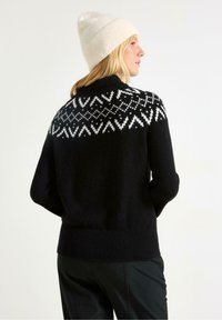 Sort sweater med hvid mønsterstrik i halsen. Strikket tekstur, lange ærmer og ribbet kant. Parret med en cremet hue.