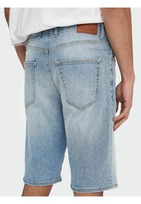 Vaaleansiniset farkkushortsit suoralla leikkauksella, joissa on kaksi takataskua ja ruskea nahkalappu vyötäröllä. Haalistunut pinta.