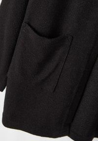 Sort strikk cardigan med detaljer som viser tekstur, en frontlomme, og en litt løs passform. Materialet ser mykt ut med en jevn overflate.
