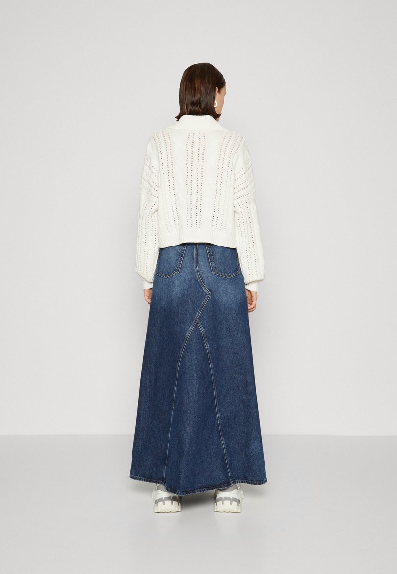 Maglione bianco lavorato a maglia con motivo testurizzato, abbinato a una lunga gonna in denim scuro con un design a cucitura curva e orlo aperto.