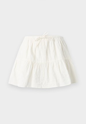 Hvit lagdelt skjørt med elastisk midjebånd og knutedetalj foran, laget av lett stoff, lagt flatt på en lys bakgrunn.