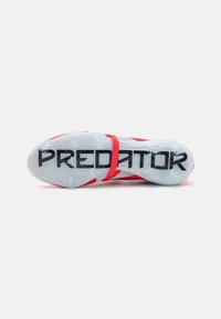 Scarpa sportiva rossa con tomaia testurizzata, fascia regolabile e suola trasparente con la scritta "PREDATOR" stampata in grandi lettere nere.