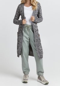 Grå och svart stickad cardigan med långa ärmar, öppen front och sidofickor; parat med ljusgröna joggingbyxor och sneakers.