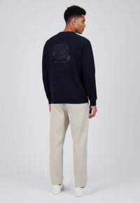 Sudadera azul marino con cuello redondo y mangas raglán, con un diseño gráfico sutil en la parte trasera. Combinada con pantalones beige claro.