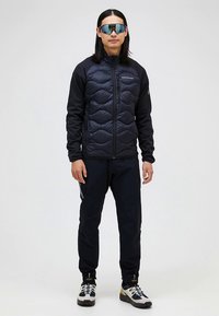 Black puffer jacket with textured quilted design, paired with black pants. Accessories include reflective sunglasses and multi-colored sneakers.