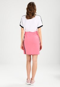 Růžová sportovní sukně s přiléhavým střihem, elastickým pasem a pruhy po stranách. Kombinována s bílým tričkem s černými detaily.