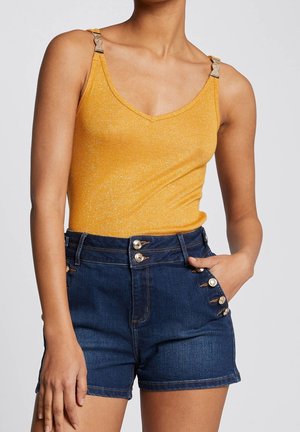 Gul metallisk tanktop med justerbare stropper og denimshorts med gulddetaljer i knapperne på siderne og en tætsiddende talje.