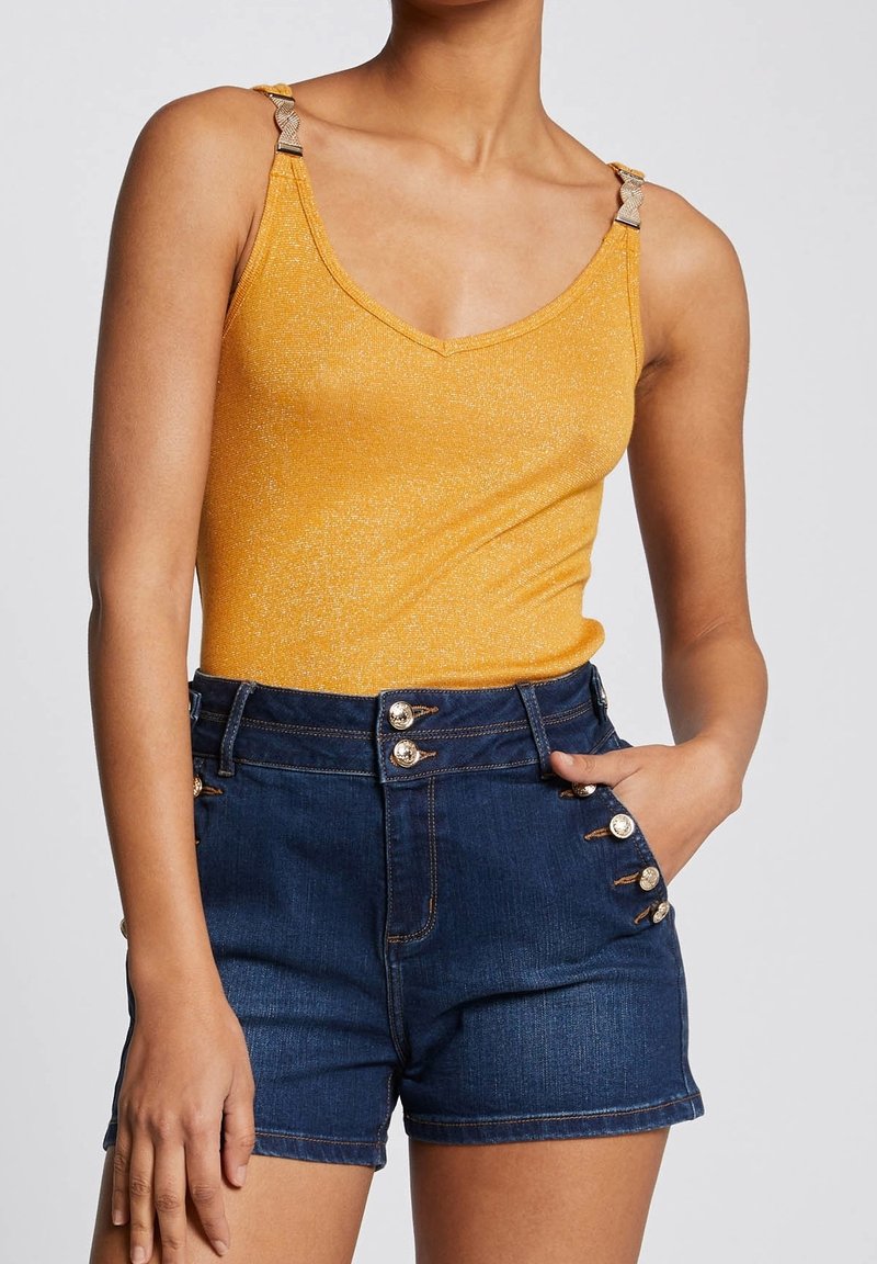 Gul metallisk linne med justerbara axelband och denimshorts med guldknappr detaljer på sidorna och en figursydd midja.