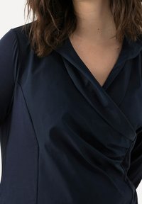 Blusa blu navy con scollatura drappeggiata e superficie liscia. Il tessuto è leggero con una leggera lucentezza e una vestibilità strutturata.
