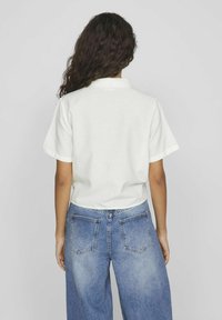 Camicia bianca a maniche corte in cotone, con colletto, abbinata a jeans blu a vita alta con tasche posteriori.