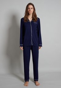 Navy blue pajama set made of soft fabric. Long-sleeved button-up top with a pocket and contrasting white piping. Loose-fitting pants.