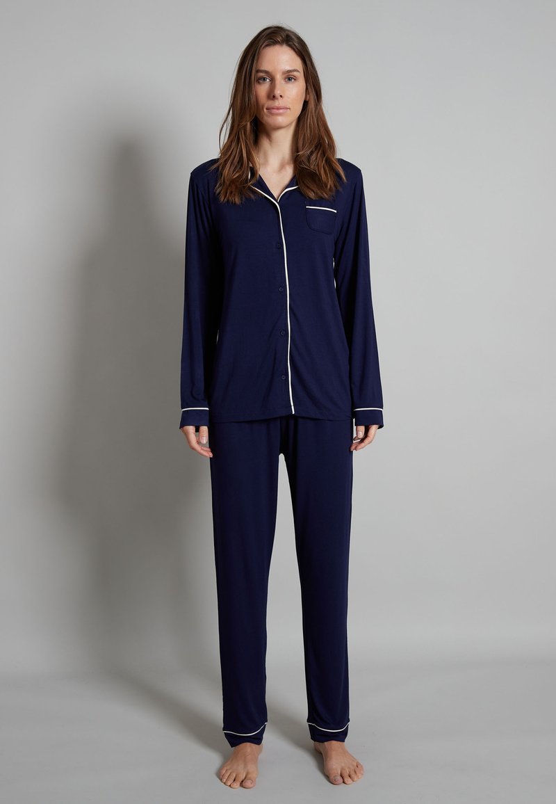 Navy blue pajama set made of soft fabric. Long-sleeved button-up top with a pocket and contrasting white piping. Loose-fitting pants.