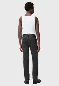 Mustat farkut suoranlahkeisella leikkauksella, joissa on takataskut ja teksturoitu pinta. Yhdistetty valkoiseen hihattomaan puseroon.