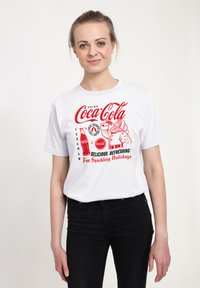Bílý bavlněný tričko s vintage grafikou Coca-Cola v červené barvě, znázorňující láhev a text „Chutné, osvěžující!“
