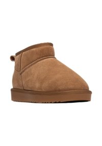 Botas de tobillo de ante en tono marrón claro, con punta redondeada, detalles de costura y suela de goma. Cuentan con una pestaña en la parte trasera para facilitarlas al ponérselas.